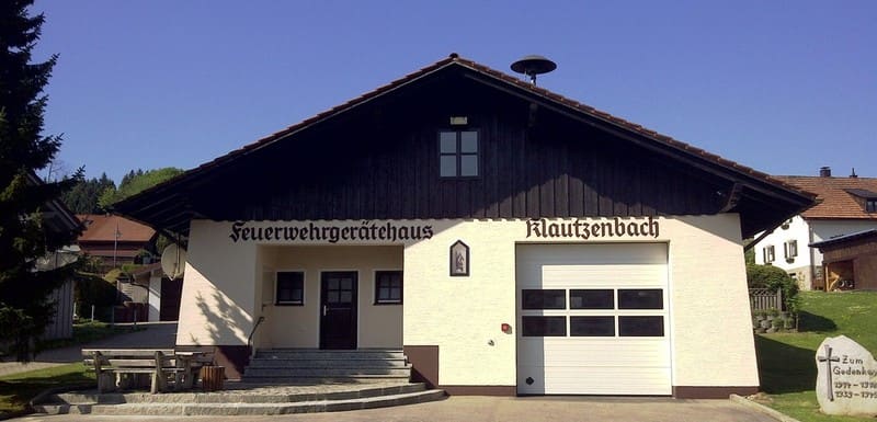 Das Gerätehaus im Irlenweg: weiße Wand, dunkler Holzgiebel, darauf gemalt „Feuerwehrgerätehaus Klautzenbach“